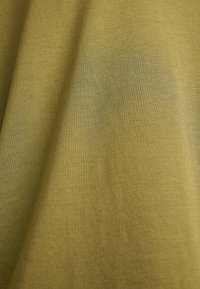 Mustard green fabric textured with a soft, smooth finish; features subtle variations in shading and a lightweight, breathable quality.