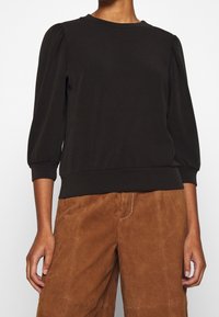 Black pullover sweater with a round neckline and puffed sleeves. Made of soft material, fitted at the waist with a smooth texture.