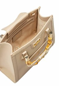 Beige leren handtas met gouden accenten, bamboe handvat en stoffen voering. Beschikt over één hoofdcompartiment, een binnenzak met rits en logo-detail.