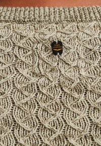 Pull en tricot texturé beige et crème, avec une étiquette noire affichant "PME LEGEND". Col côtelé.