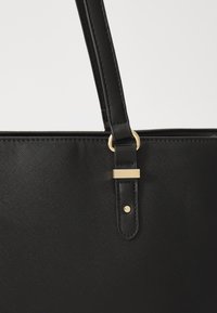 Schwarze synthetische Tragetasche mit strukturierter Oberfläche, ausgestattet mit einem goldfarbenen Metalldetail und einem stabilen schwarzen Schultergurt.