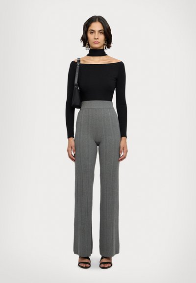 Top lung negru, cu mâneci lungi și design off-the-shoulder, asortat cu pantaloni largi gri texturat, cu talie înaltă și sandale negre.