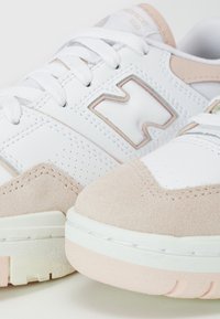 Gros plan sur des baskets New Balance blanches et beiges montrant les lacets, le logo et les bouts en daim texturé.