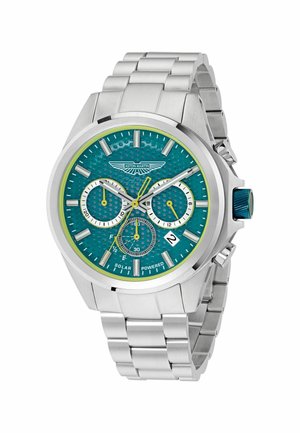 Reloj de acero inoxidable plateado con esfera texturizada en color verde azulado, detalles en amarillo, tres subesferas, ventana de fecha y corona azul. Mecanismo solar.