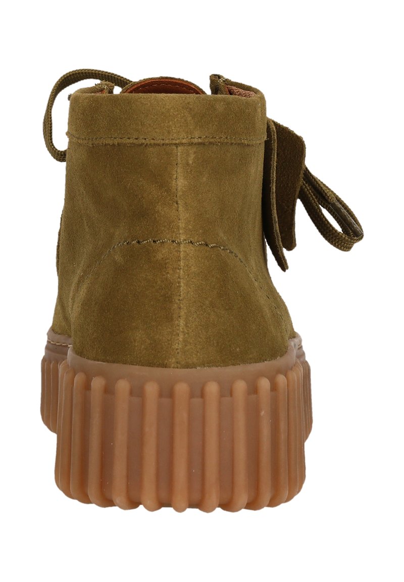 Botas de ante verde oliva hasta el tobillo con puntas redondeadas y una suela de goma gruesa y translúcida que presenta estrías verticales. La vista trasera muestra una etiqueta de tela.
