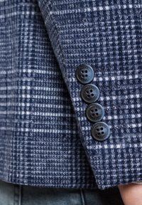 Niebieska marynarka w kratkę z wełnianą teksturą, z czterema czarnymi guzikami na mankietach, z subtelnym wzorem w różnych odcieniach.