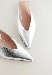 Escarpins argentés à bride arrière avec un design à bout pointu, finition métallisée texturée et un talon bas. L'intérieur présente une doublure douce de couleur claire.