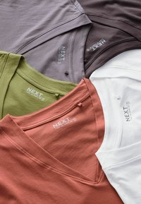 Cuatro camisetas de cuello en V en marrón, blanco, verde oliva y terracota. Fabricadas en suave algodón, con una etiqueta que muestra el nombre de la marca.