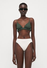 Top bikini strutturato verde scuro con spalline sottili, abbinato a culotte bikini bianche strutturate a vita alta. Gli occhiali da sole completano il look.