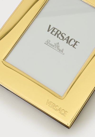 Ορθογώνιο χρυσό πλαίσιο φωτογραφίας με το "Versace" χαραγμένο στο κάτω άκρο και μια κάρτα υποκατάστασης με το κείμενο "Versace Rosenthal." στο εσωτερικό