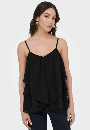 Žena s tmavými vlasmi po plecia, ktorá nosí zlaté kruhové náušnice a voľný čierny vrstvený top bez rukávov s tenkými ramienkami.