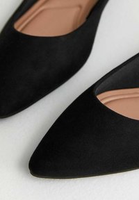 Svarta mocka spetsiga ballerinas med en böjd utskärning vid vampen, med en slät beige sula och en tunn, minimalistisk svart ytsula.