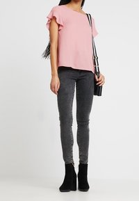 Haut à manches courtes rose avec des bords froncés, associé à un jean skinny noir et des bottines noires. L'accessoire comprend un petit sac à bandoulière.