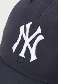 Navy baseball cap with a white embroidered "NY" logo, featuring a structured design and smooth fabric texture. Seam detail visible.