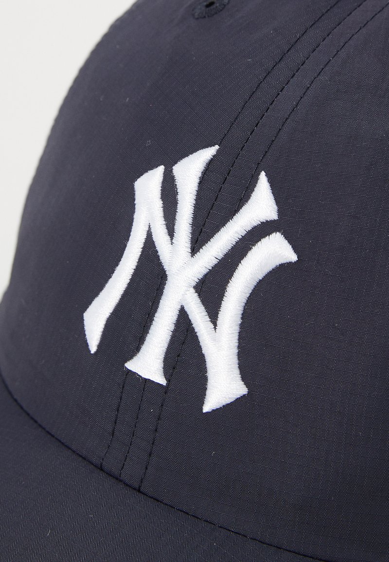 Marineblauwe baseballpet met een witte geborduurde "NY"-logo, met een gestructureerd ontwerp en een gladde stoftextuur. Naaddetails zichtbaar.