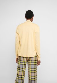 Maglione giallo a maglia con scollo rotondo e polsini a coste, abbinato a pantaloni in plaid nei toni del grigio, giallo e nero.