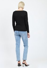 Top nero a maniche lunghe abbinato a jeans azzurri chiari. I jeans sono leggermente svasati; l'outfit è completato da tacchi neri con cinturini e motivi.