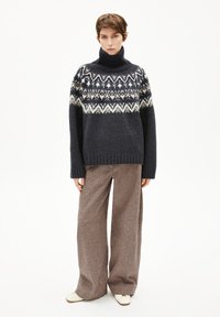 Marineblau gestrickter Rollkragenspullover mit Fair Isle-Muster in Creme und Beige, kombiniert mit beigen weitem Hosen und cremefarbenen Schuhen.