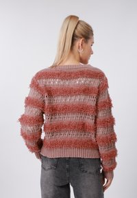 Πλεκτό πουλόβερ με υφή σε ανοιχτό ροζ χρώμα με σκούρες ροζ χνουδωτές ρίγες. Ανοιχτή πλέξη, ριμπ μανσέτες και τελείωμα, φορεμένο με γκρι τζιν.