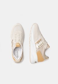 Baskets beiges avec une tige texturée, des accents en daim, des détails métalliques et une semelle intermédiaire blanche. Lacets et détail du logo inclus.