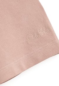 Różowa tkanina bawełniana o teksturowanym splocie, z delikatnym haftowanym logo "Polo Club" w jaśniejszym odcieniu. Krawędzie starannie wykończone.