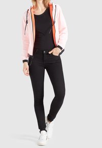 Lekka, różowo-czarna kurtka z kapturem z zamkiem, noszona na czarnej koszulce, połączona z czarnymi obcisłymi dżinsami i białymi sneakersami.