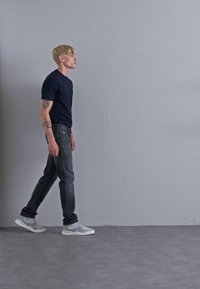 Navy T-shirt, grey denim jeans, and light grey athletic shoes; casual outfit with a fitted silhouette and minimal design details.