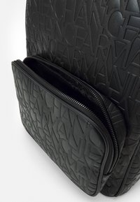 Zaino nero con motivo di logo impresso, materiale texture, doppie tasche con zip e bordi lisci per una facile maneggevolezza.