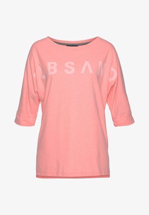 Chemise rose ample avec manches trois-quarts et lettres blanches pâles sur la poitrine formant un motif de texte stylisé.