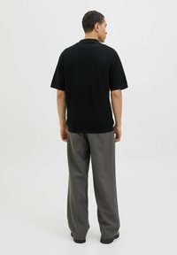 Black short-sleeve polo shirt with a textured knit design, paired with loose-fitting gray trousers and black footwear. Simple and modern aesthetic.