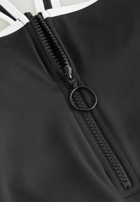 Mustaline ujumisriided, millel on valge äär, keskosas on ringikujuline tõmblukk, valmistatud sileda ja mattpinnaga materjalist.