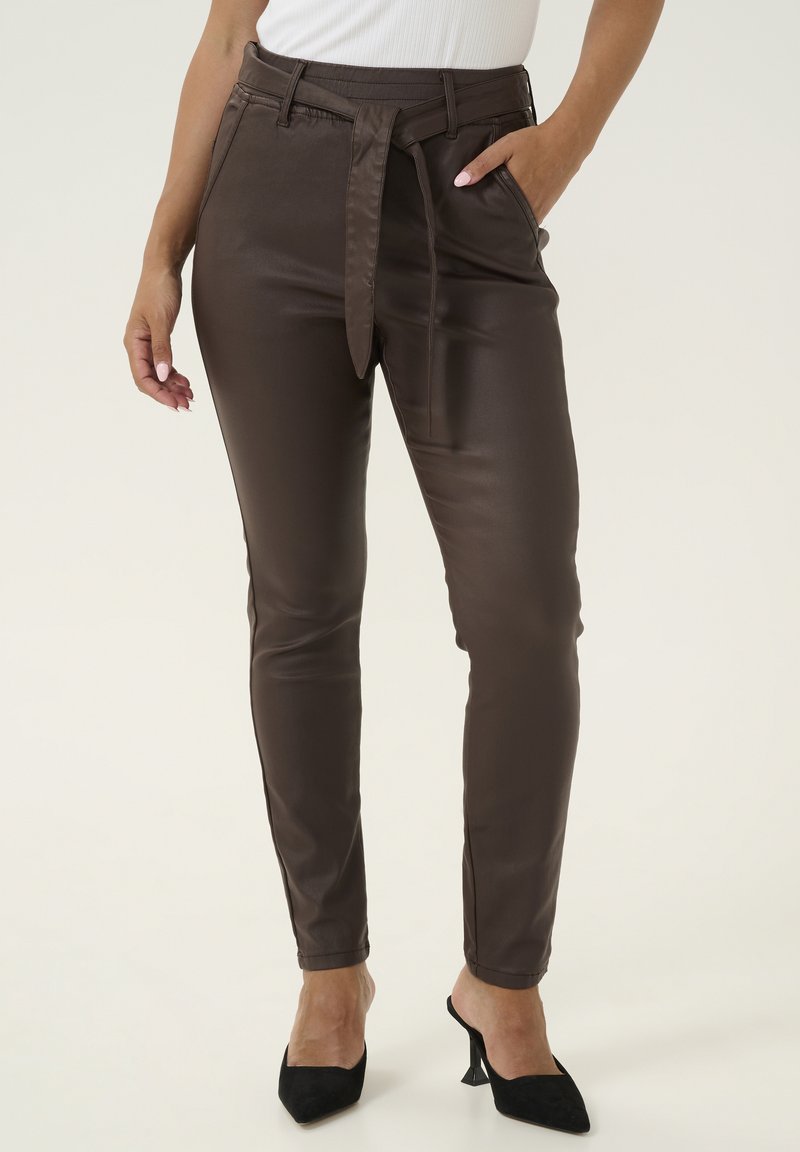 Bruine synthetische slim-fit broeken met een ceintuur in de taille, zijzakken en een gladde textuur. Gdragend met zwarte puntige hakken.