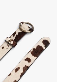 Cinturón de estampado animal hecho de pelo suave con una base beige y manchas marrón oscuro, que cuenta con un lazo metálico y un acento de calavera en la correa.