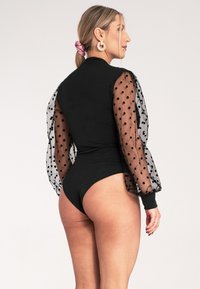 Czarny body z przezroczystymi rękawami w kropki, dopasowany fason i subtelna tekstura. Akcenty obejmują mankiety i okrągły dekolt na plecach.