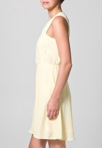 Vestido amarillo sin mangas con una cintura ajustada, falda fluida y textura de tela suave. Diseño simple sin adornos ni estampados.