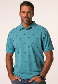 Turkusowa koszulka polo z kołnierzykiem, z powtarzającym się wzorem palm w ciemnoniebieskim kolorze. Krótkie rękawy i miękka faktura. Noszona z dżinsami.