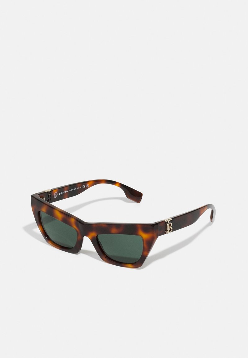 Tortoiseshell saulesbrilles ar leņķainām rāmēm, zaļiem stikliem un zelta akcentu uz tempļa. Tekstūrēts materiāls ar spīdīgu apdari.