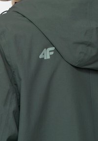 Mørkegrøn jakke med mat finish, med hætte og et diskret trykt logo (4F) på ryggen. Glat tekstur, letvægtig design.