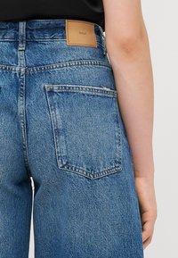 Hoch taillierte blaue Jeans aus Denim mit einem Lederpatch an der Rückseite, das "ONLY" beschriftet ist. Sie verfügen über ein klassisches Fünf-Taschen-Design und fransige Kanten.
