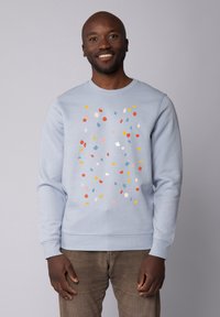 Sweatshirt bleu clair avec un motif éparpillé coloré en rouge, jaune et teintes pastel. Dispose d'une encolure ras du cou et de poignets côtelés.