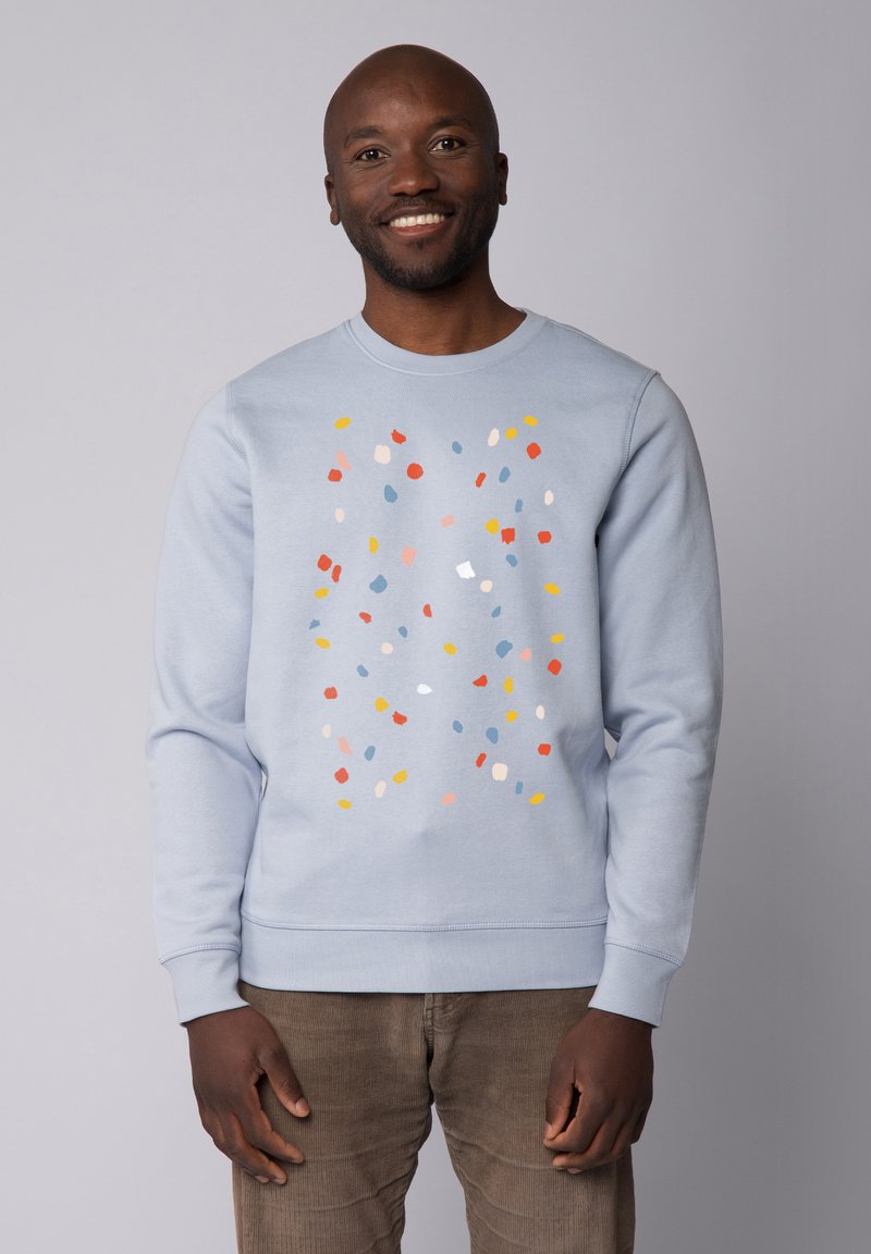 Sweatshirt bleu clair avec un motif éparpillé coloré en rouge, jaune et teintes pastel. Dispose d'une encolure ras du cou et de poignets côtelés.