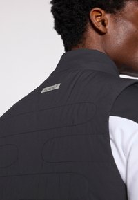 Must mustrakk, millel on kõrge krae, tekstureeritud tikand ja hõbedane silt "FUROR7" taga. Sujuv kangas ja minimalistlik disain.