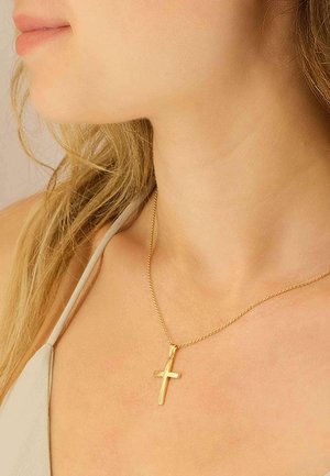 Collier pendentif croix couleur or sur une chaîne fine, porté près de la clavicule, avec une surface lisse et un design minimaliste.