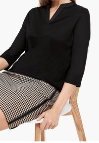 Zwarte top met een V-hals en 3/4 mouwen, gemaakt van gladde stof. Gepaarde met een rok in hounds-tooth patroon met een zwarte rand.