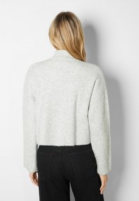 Grå ribbad kort tröja med hög krage och lösa ärmar, tillverkad av mjukt material. Buren med svarta byxor med en avslappnad passform.