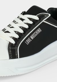 Baskets Love Moschino noir et blanc avec lacets blancs, œillets noirs et semelle blanche épaisse sur un fond clair.
