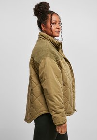 Polstret quilted jakke i oliven grønn med en hyggelig krage. Har knappefront, sidelommer og en avslappet passform.