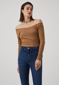 Top castanho canelado, sem ombros, combinado com jeans azuis de cintura alta, com fecho de botão e bolsos laterais. Textura suave e design ajustado.