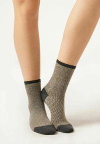 Socken mit Hahnentrittmuster in Beige und Schwarz, mit gerippten Bündchen. Verstärkter Fersen- und Zehenbereich. Knöchellang, weiche Textur.