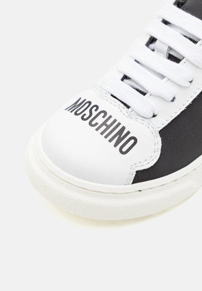 Zapatilla en blanco y negro con una puntera de cuero blanco con la impresión "MOSCHINO", lados de tela negra y cordones blancos. Suela de goma texturizada.